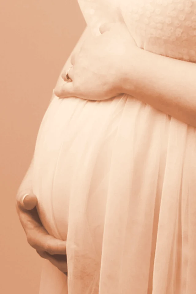 Femme enceinte tenant son ventre, tons chauds crème et terracotta